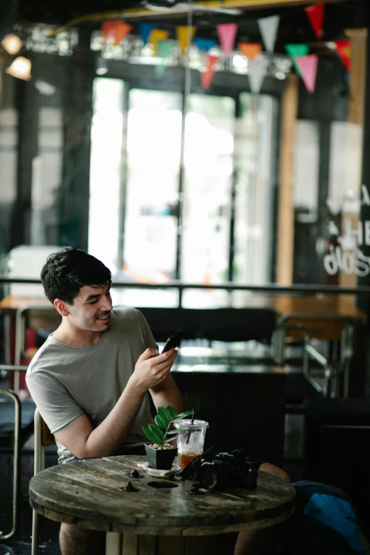 a man sitting at a table looking at his cell phone, pexels contest winner, happening, square, young spanish man, gif, large)}]