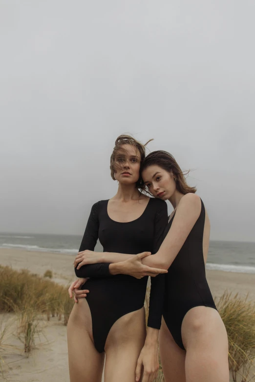 two women standing next to each other on a beach, unsplash, renaissance, wearing a black bodysuit, overcast, wearing leotard, ignant