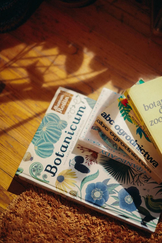 a pile of books sitting on top of a wooden table, botanicals, labels, polish, sun is shining