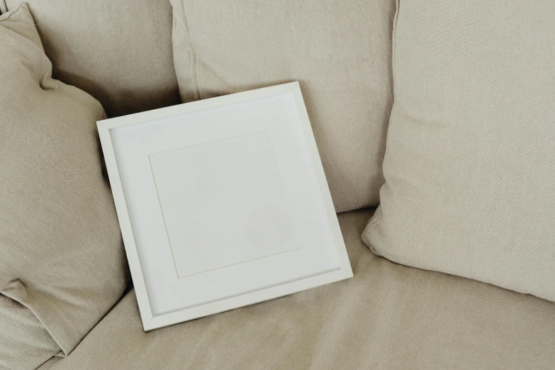 a picture frame sitting on top of a couch, inspired by Agnes Martin, pexels contest winner, john pawson, silver，ivory, square shapes, white floor