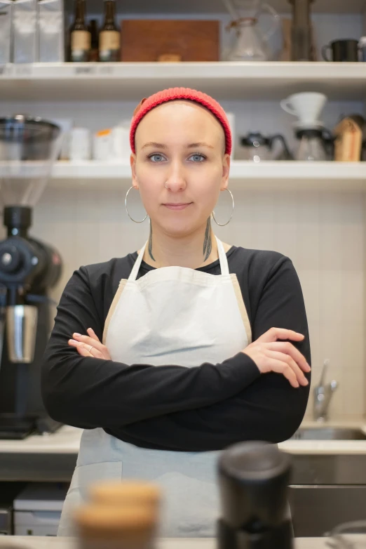a woman standing in a kitchen with her arms crossed, a portrait, inspired by Louisa Matthíasdóttir, pexels contest winner, aussie baristas, shaved head, starbucks aprons and visors, headshot profile picture