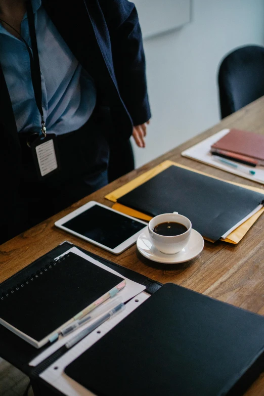 a wooden table topped with notebooks and a cup of coffee, trending on unsplash, private press, wearing black business suit, standing on a desk, someone lost job, executive industry banner