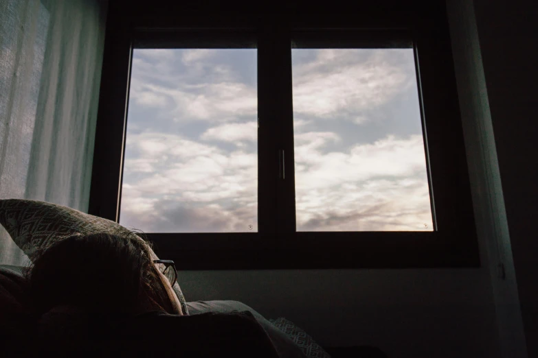 a person laying on a bed in front of a window, a picture, inspired by Elsa Bleda, unsplash, romanticism, altostratus clouds, late summer evening, tv still frame, low angle facing sky