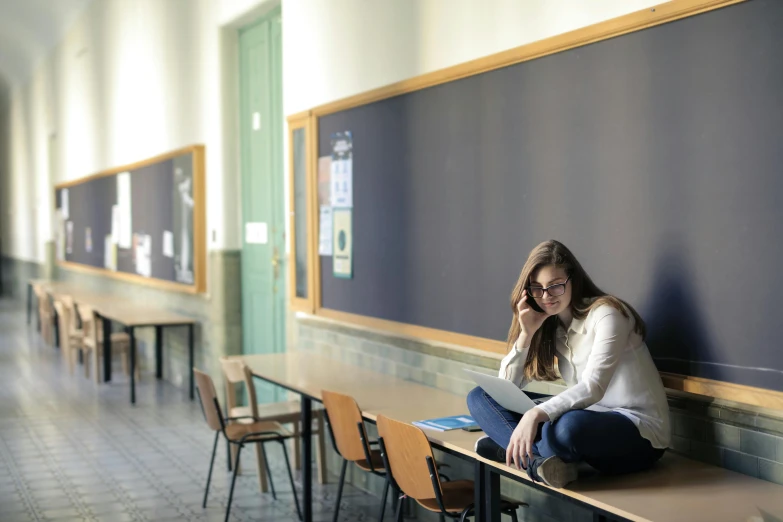 a woman sitting on a bench in front of a blackboard, pexels, in school hallway, background image, multiple stories, aged 13