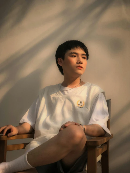 a young man sitting on top of a wooden chair, a polaroid photo, inspired by Huang Gongwang, pexels contest winner, realism, white t - shirt, (golden hour), genderless, off - white collection