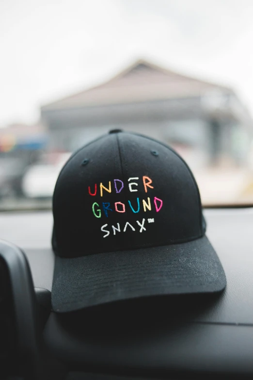 a hat sitting on the dashboard of a car, an album cover, inspired by Okuda Gensō, trending on pexels, graffiti, slay, truncated snout under visor, with text, ground up angle