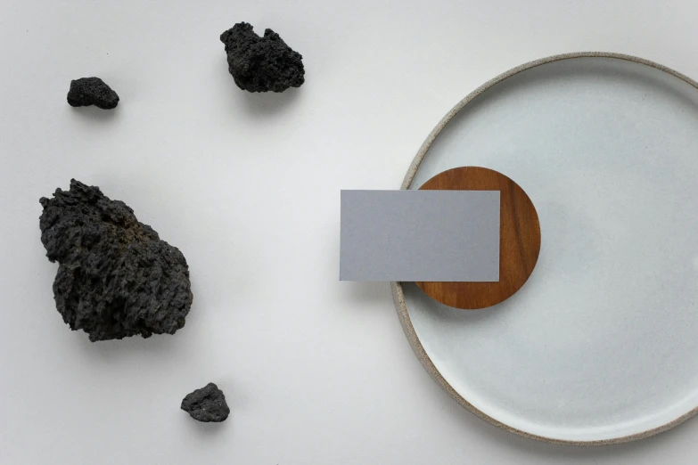 a white plate sitting on top of a white table, an abstract sculpture, inspired by Matteo Pérez, unsplash, igneous rock materials, business card, terraforming jezero crater, on a wooden plate