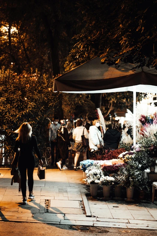 a group of people walking down a sidewalk at night, flowers, markets, lush surroundings, header