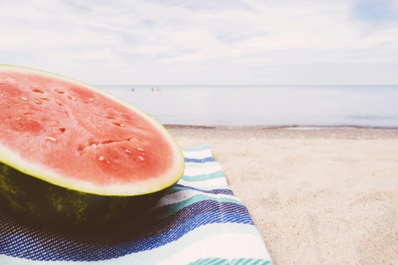 a watermelon sitting on top of a towel on a beach, an ocean, at the sea