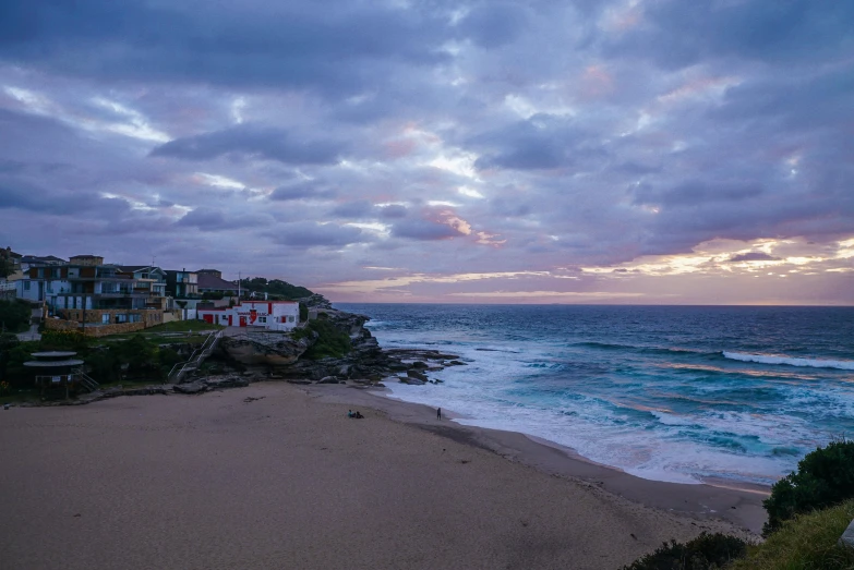 a bench sitting on top of a sandy beach next to the ocean, bondi beach in the background, cliff side at dusk, profile image, conde nast traveler photo