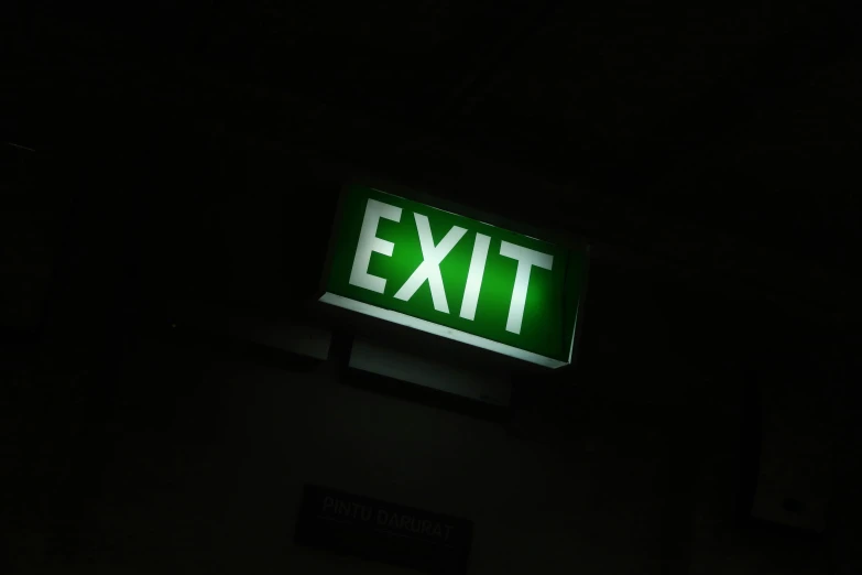 a green exit sign lit up in the dark, a photo, pexels, happening, 9/11, indoor picture, dark and white, operation