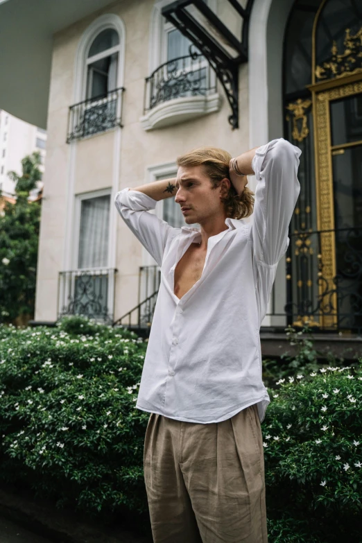 a man in a white shirt standing in front of a building, trending on unsplash, renaissance, non binary model, johan liebert, lush surroundings, joe keery