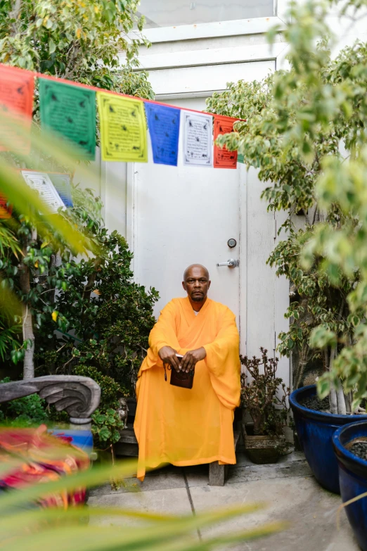 a man in a yellow robe standing in front of potted plants, sukhasana, bay area, wearing jedi robes and a sari, 2022 photograph
