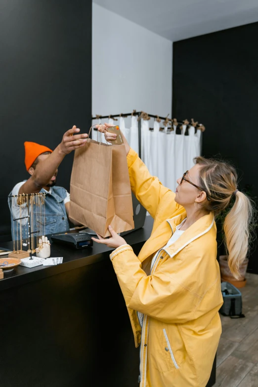 a couple of people that are standing in a room, at checkout, holding a gold bag, on high-quality paper, wearing a yellow hoodie