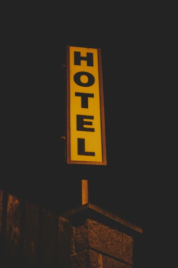 a hotel sign sitting on the side of a building, an album cover, unsplash, dim lit, yellow, ((rust)), gif