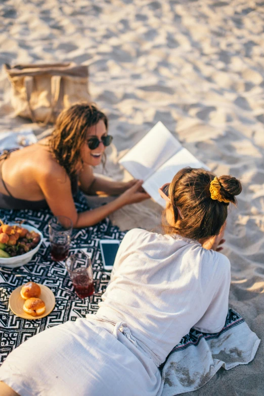 a couple of women sitting on top of a sandy beach, food, reading a book, millennial vibes, uncropped