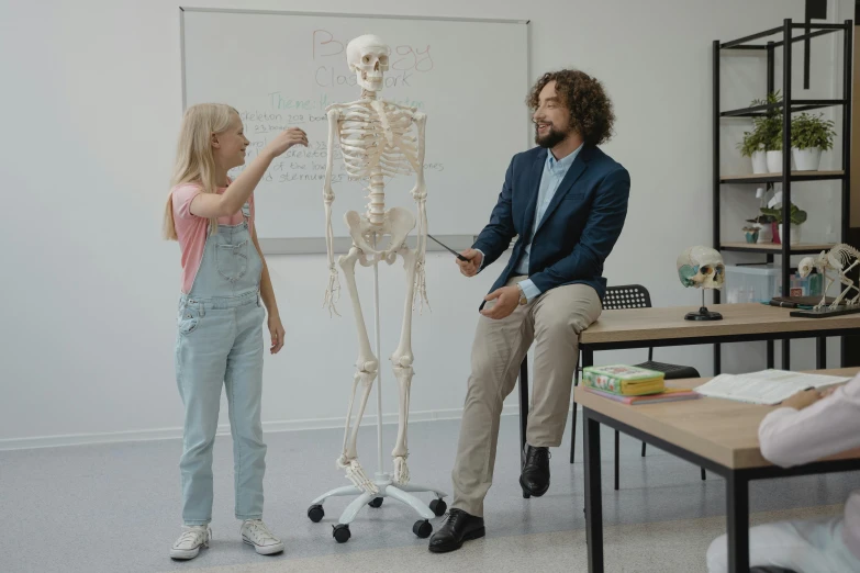 a man and a woman standing in front of a skeleton, a cartoon, pexels contest winner, academic art, sitting in the classroom, scene from live action movie, shot on canon eos r5, simple anatomic