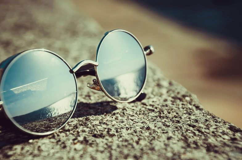 a pair of sunglasses sitting on top of a rock, unsplash, photorealism, silver，ivory, round glasses potter, retro stylised, at the seaside