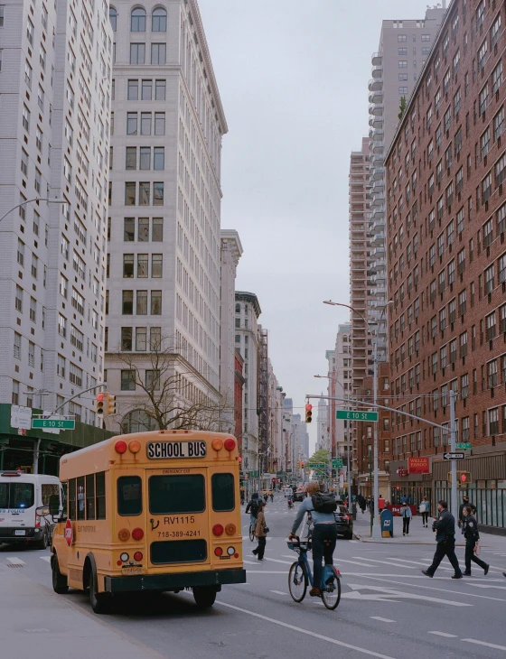 a yellow school bus driving down a street next to tall buildings, by Carey Morris, pexels contest winner, manhattan, white marble buildings, background image, people on the streets