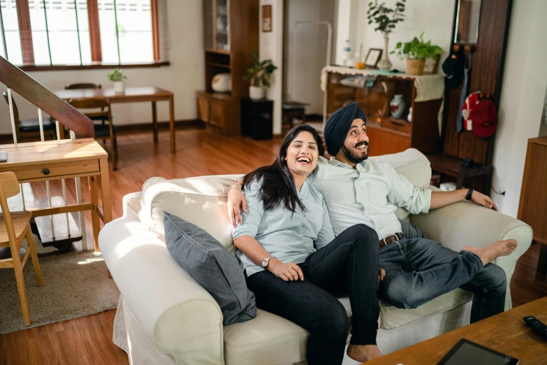 a man and woman sitting on a couch in a living room, inspired by Manjit Bawa, pexels contest winner, watching tv, both laughing, australian, long shot view