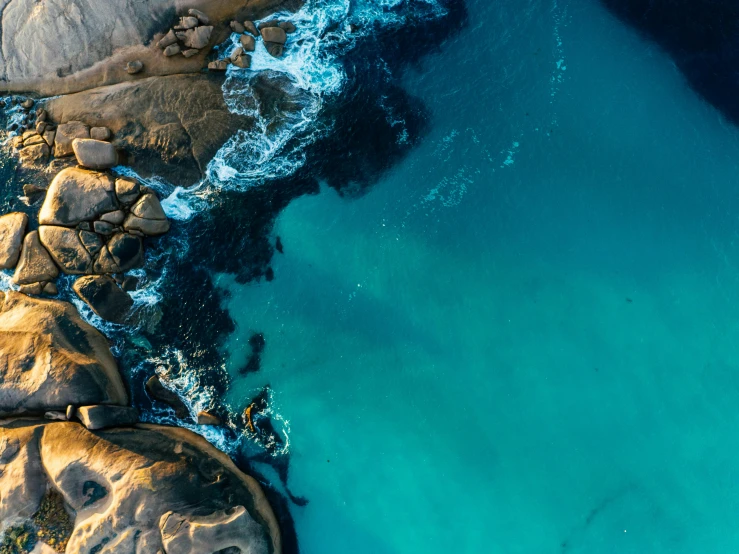 an aerial view of a body of water surrounded by rocks, by Lee Loughridge, pexels contest winner, teal skin, australian beach, slight glow, black