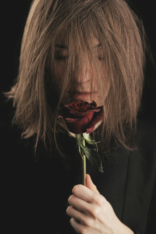 a woman holding a rose in front of her face, an album cover, inspired by Nicola Samori, trending on unsplash, johan liebert mixed with alucard, unkept hair, paul barson, yohji yamamoto