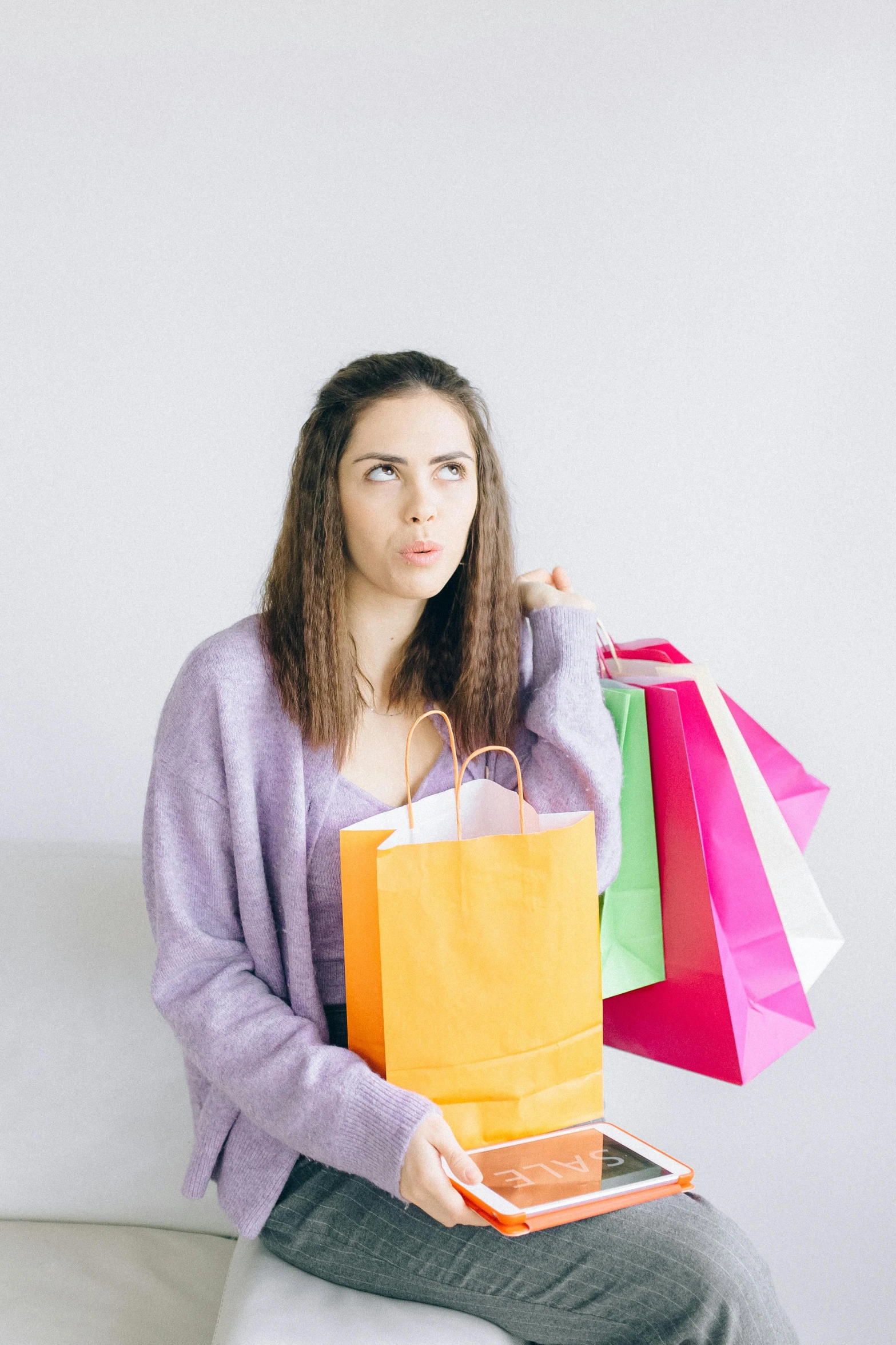 a woman sitting on a couch holding shopping bags, a colorized photo, pexels, upset, on grey background, pastel clothing, young woman looking up