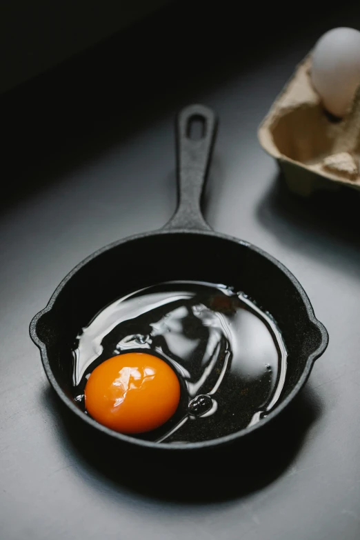 an egg in a frying pan next to a carton of eggs, trending on pexels, dark kitchen of an art student, black fork, molten, an orange