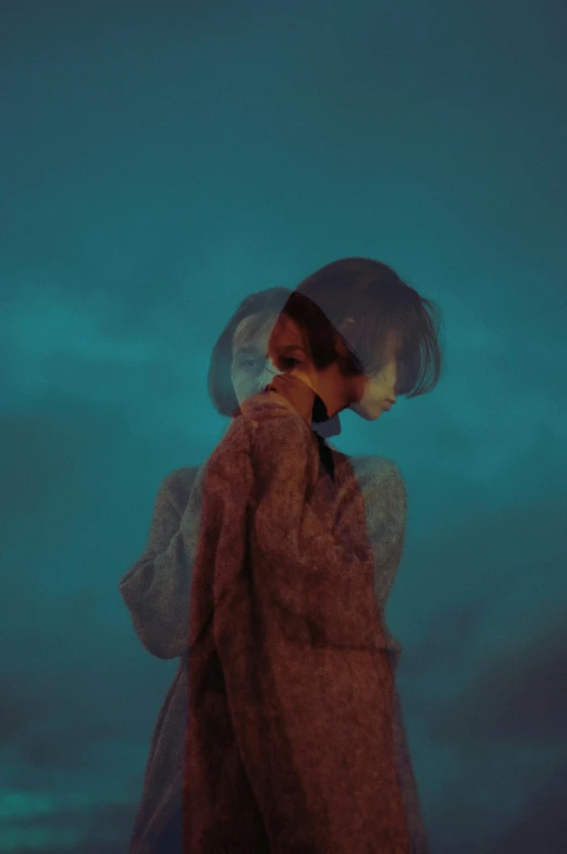 a woman standing on top of a beach next to the ocean, an album cover, inspired by Elsa Bleda, trending on pexels, magical realism, cloak covering face, cold blue colors, reflection, (night)