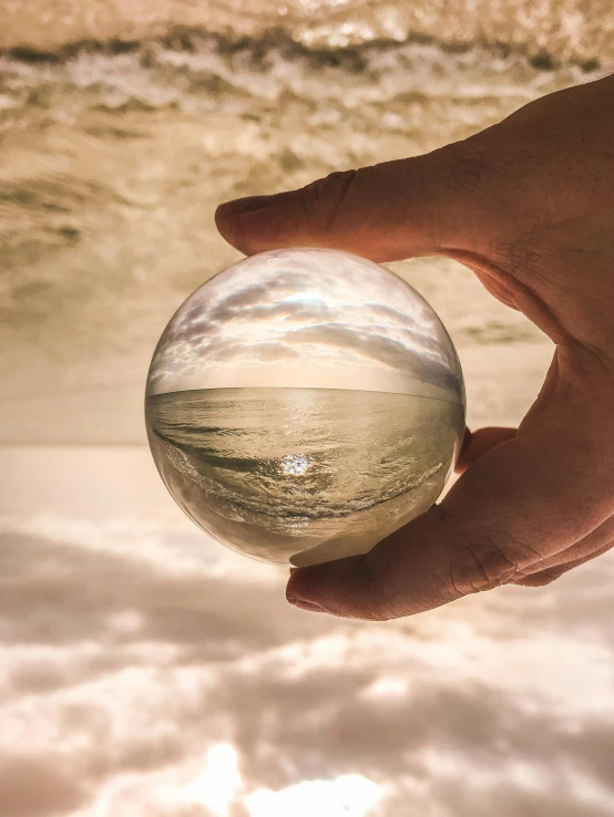 a person holding a crystal ball in their hand, inspired by Beeple, unsplash contest winner, magical realism, ocean view, today\'s featured photograph 4k, realistic glass sculpture, perspective from below