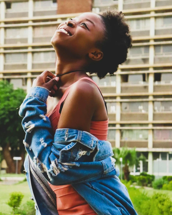 a woman standing in front of a tall building, trending on unsplash, happening, super cute funky black girl, grinning lasciviously, lgbtq, jean jacket