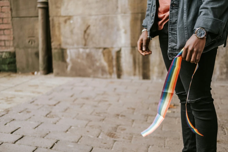 a man standing on a brick sidewalk holding a rainbow ribbon, trending on pexels, lesbians, beautiful city black woman only, ribbon chapel, zoomed in