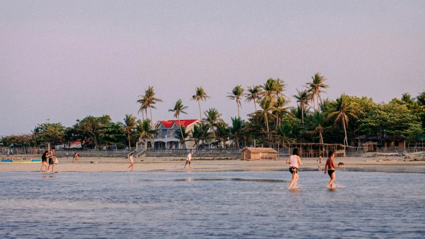 a group of people standing on top of a sandy beach, coconut trees, white buildings with red roofs, playing soccer at the beach, unsplash photography