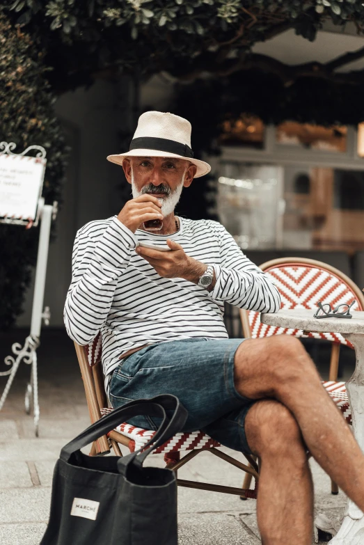 a man sitting in a chair using a cell phone, white straw flat brimmed hat, grey trimmed beard, wearing stripe shirt, style of paolo parente