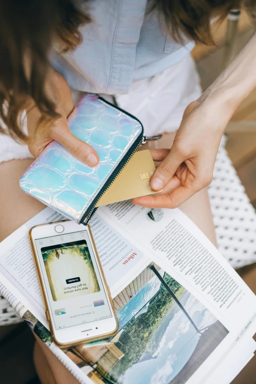 a woman sitting on a bench with a book and cell phone, a picture, by Julia Pishtar, trending on pexels, holographic case display, cyan and gold scheme, holding ace card, flatlay book collection