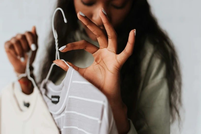 a close up of a person holding a shirt on a hanger, a photo, by Matija Jama, trending on pexels, painted nails, african american young woman, hand gesture, thumbnail