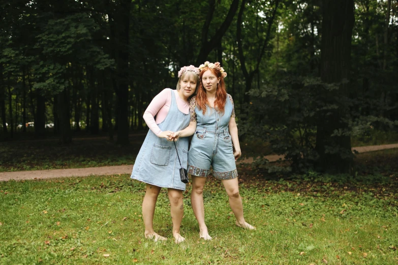 a couple of women standing on top of a lush green field, inspired by Diane Arbus, pexels, blue overalls, costume, in the wood, medium format