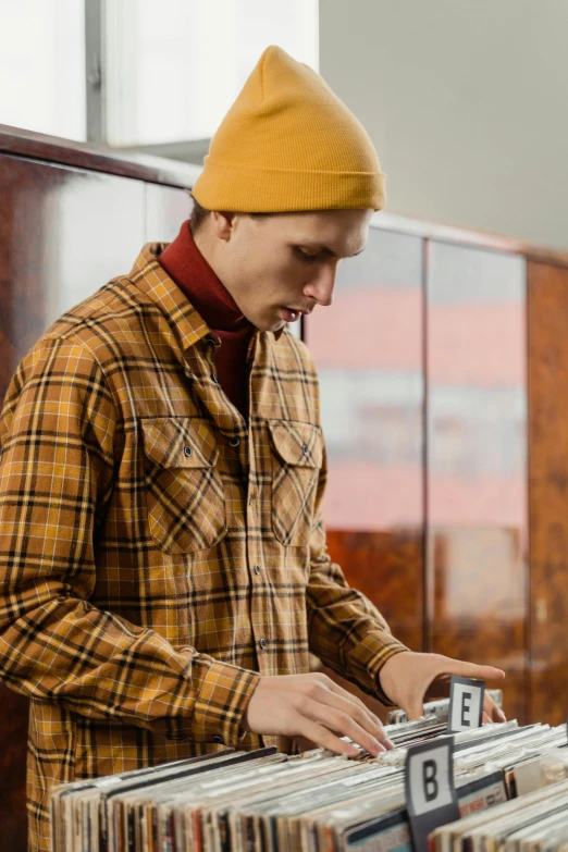 a man standing next to a pile of records, trending on pexels, wearing plaid shirt, beanie, attractive male playing piano, thumbnail