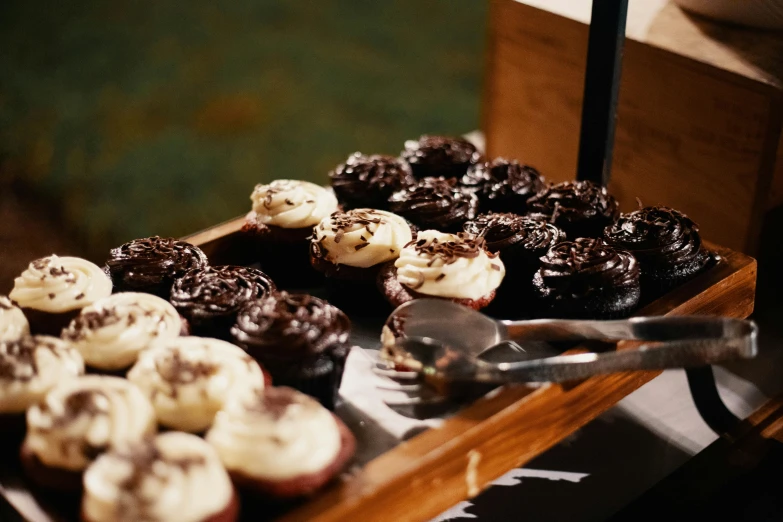 a close up of a tray of doughnuts on a table, by Joe Bowler, trending on unsplash, hurufiyya, cupcake, dark chocolate hair colour, overflowing feast buffet table, dark and white