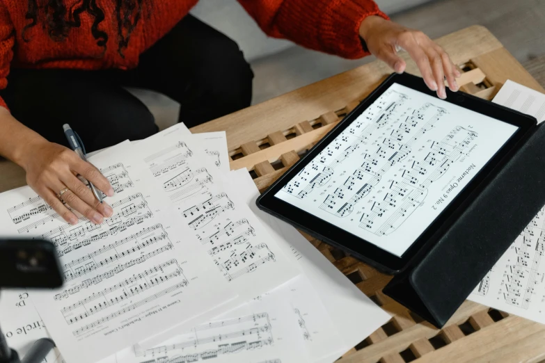 a tablet computer sitting on top of a wooden table, an album cover, by Robert Medley, pexels, analytical art, sheet music, hands, sketching, christina kritkou