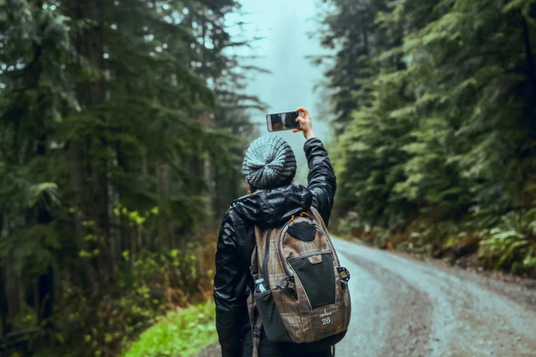 a person with a backpack taking a picture of a road, by Carey Morris, pexels contest winner, enjoying a stroll in the forest, hold up smartphone, 🚿🗝📝