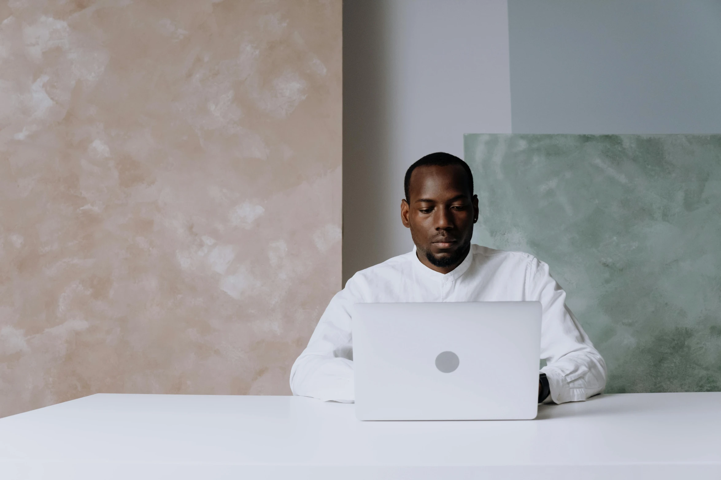 a man sitting at a table with a laptop, by Carey Morris, pexels contest winner, an all white human, ( ( dark skin ) ), white backround, elegant shot