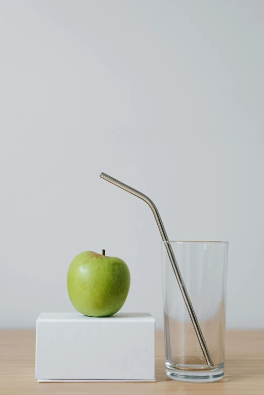 an apple and a glass of water on a table, a still life, unsplash, minimalism, made of brushed steel, straw, 9, side profile view