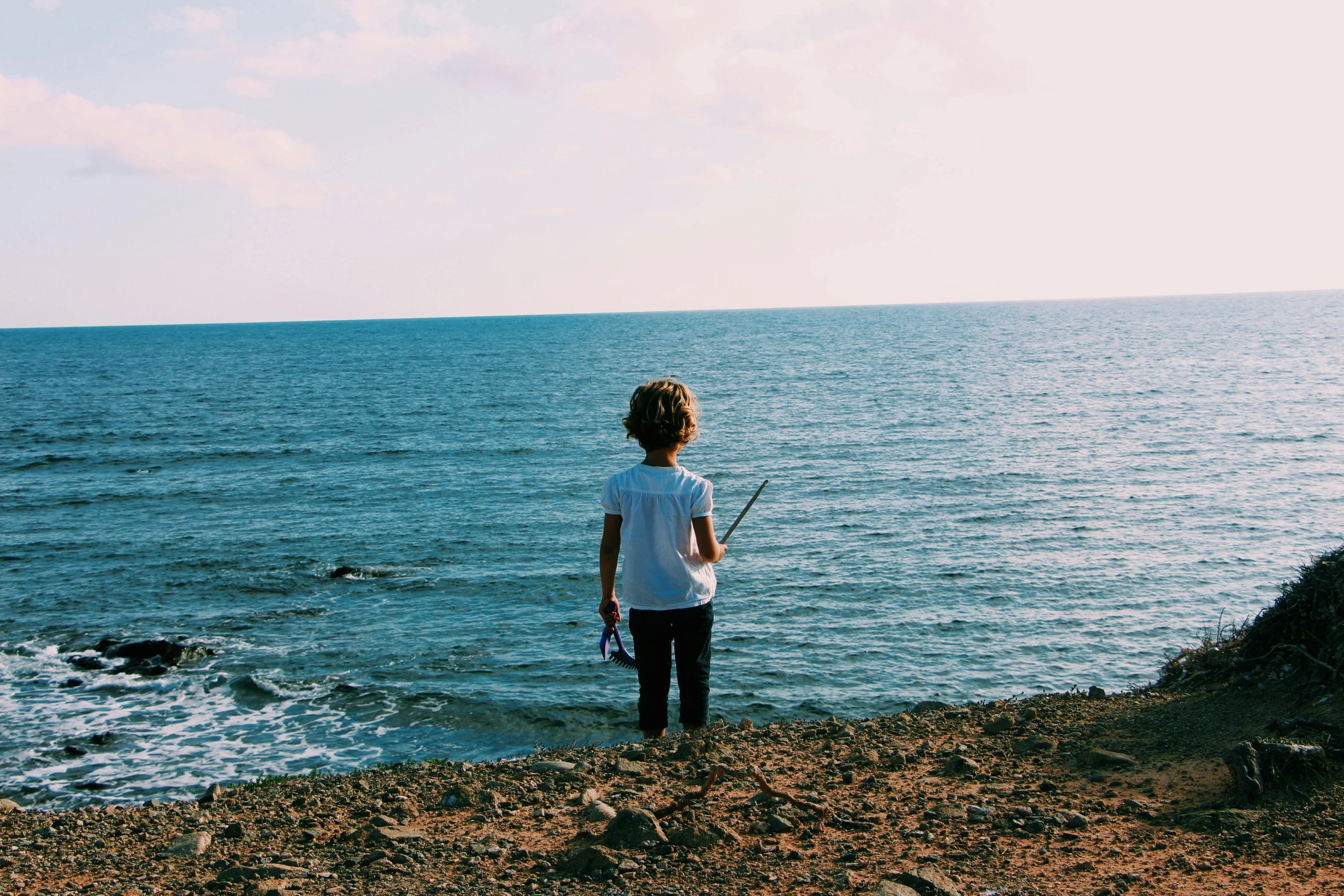 a little boy standing on top of a beach next to the ocean, pexels contest winner, fishing pole, girl standing on cliff, facing away, next gen