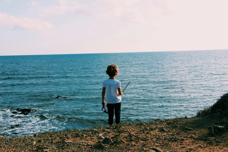 a little boy standing on top of a beach next to the ocean, pexels contest winner, fishing pole, girl standing on cliff, facing away, next gen