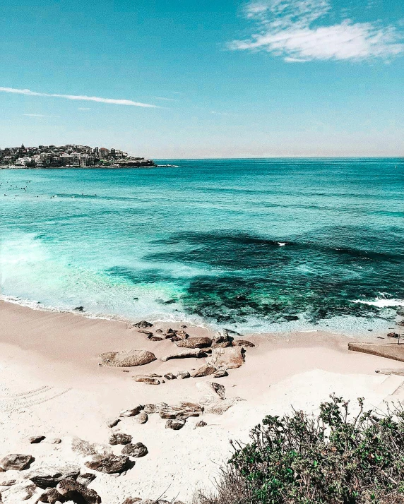 a large body of water next to a sandy beach, by Sydney Carline, with instagram filters, city of pristine colors, light blue water, coastal