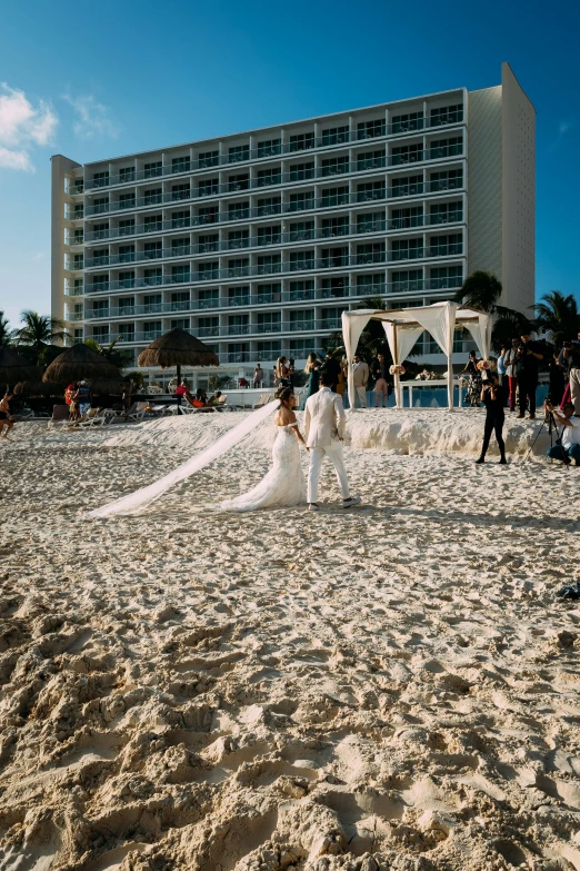 a couple of people standing on top of a sandy beach, with walkways, bride and groom, roaming the colony, laying on beach