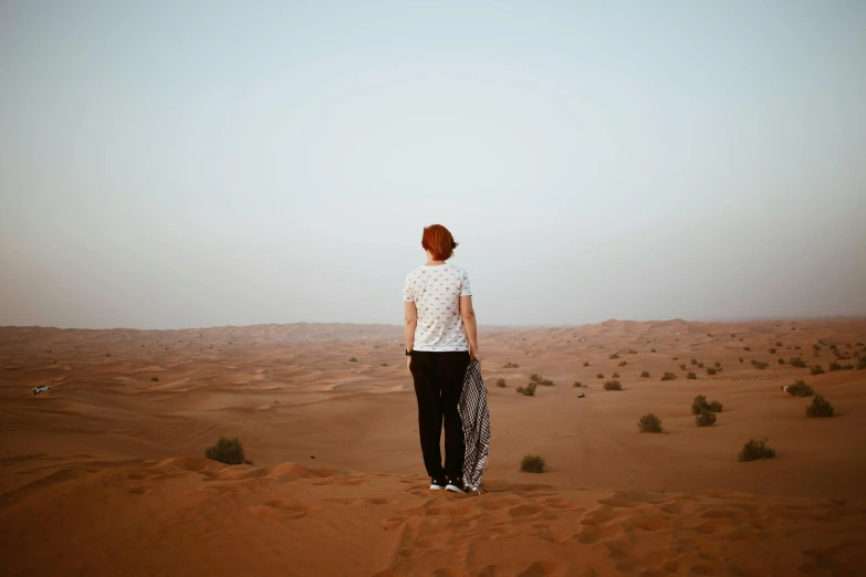 a person standing in the middle of a desert, by Anna Findlay, pexels contest winner, looking off into the distance, middle eastern, dunes in the background, heartbreak