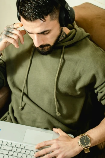 a man sitting in a chair with a laptop and headphones, a colorized photo, trending on pexels, beige hoodie, olive green, thumbnail, military clothing