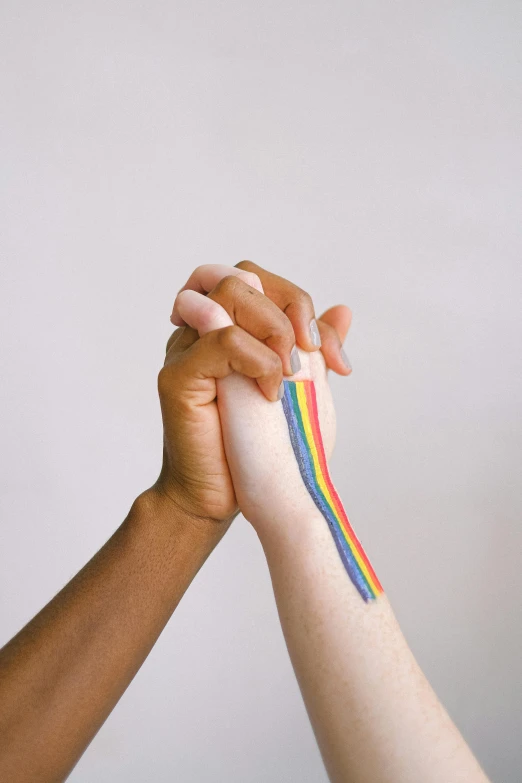 two people holding hands with a rainbow painted on them, trending on pexels, white bandage tape on fists, diverse, striped, holding trident